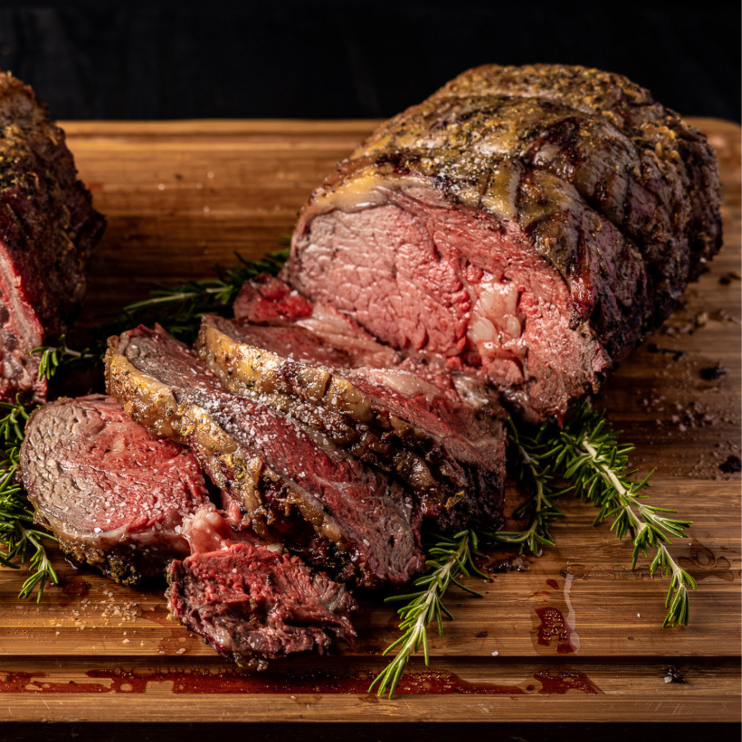 Smoked Prime rib on a wooden cutting board. The prime rib is sliced open, showing the inside of the meat.
