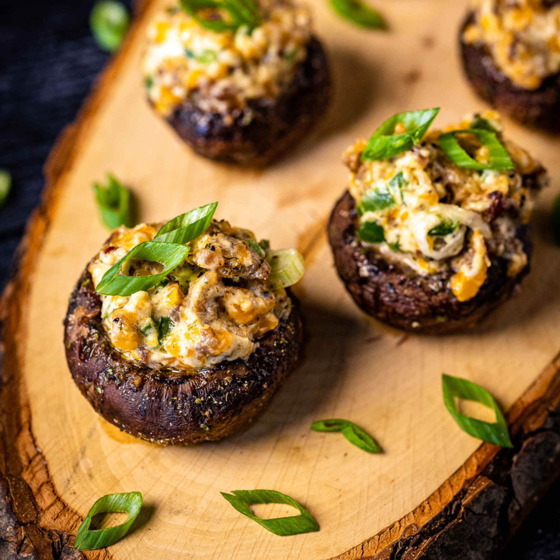 Four stuffed mushrooms on a wooden cutting board. The mushrooms were seasoned with Hey Grill Hey Fish and Veggie Rub.