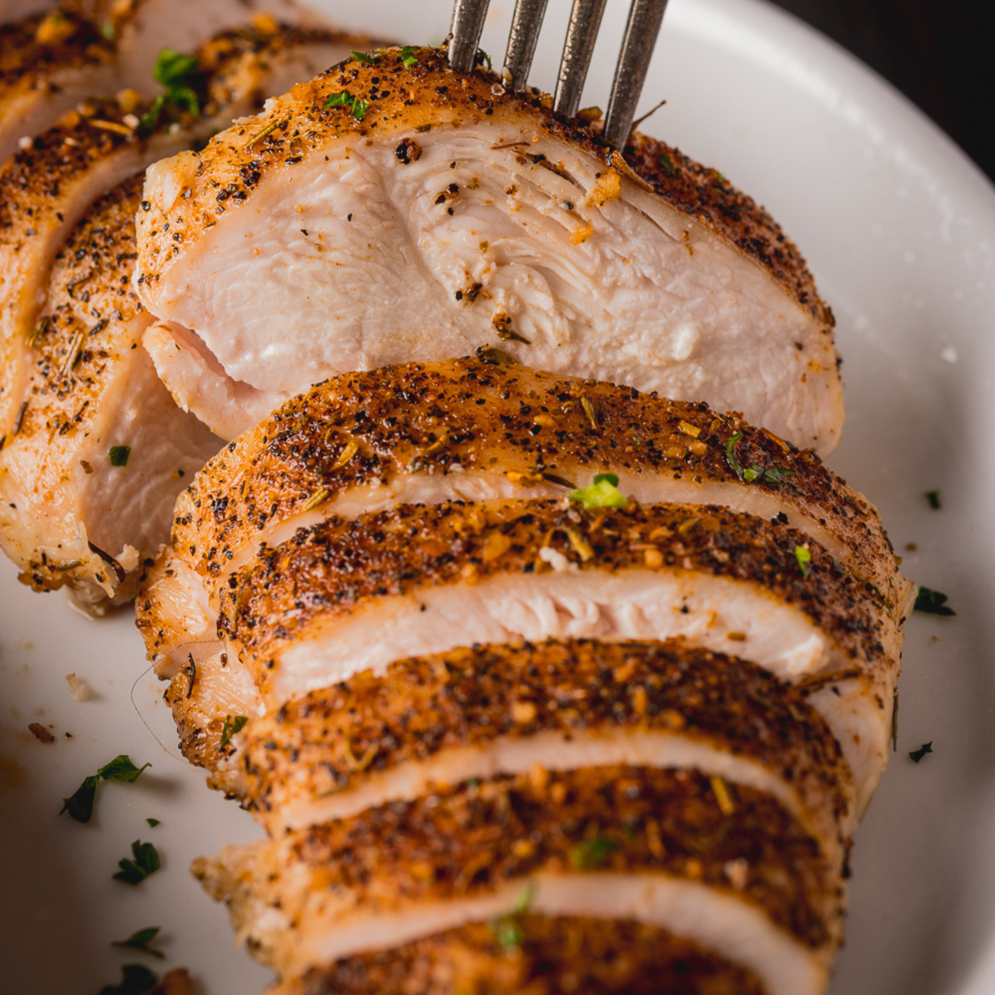 Close up photo of cooked Chicken breast prepared with Hey Grill Hey Chicken rub, sliced, and placed on a white plate. 