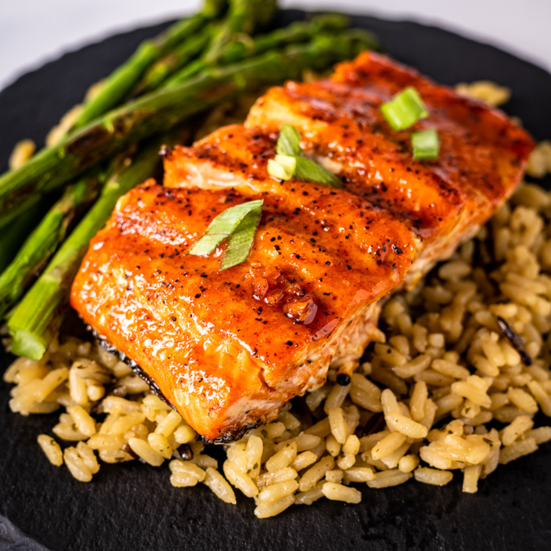 A piece of grilled or smoked salmon, glazed with Maple Bourbon BBQ Glaze, sitting on a bed of rice. 